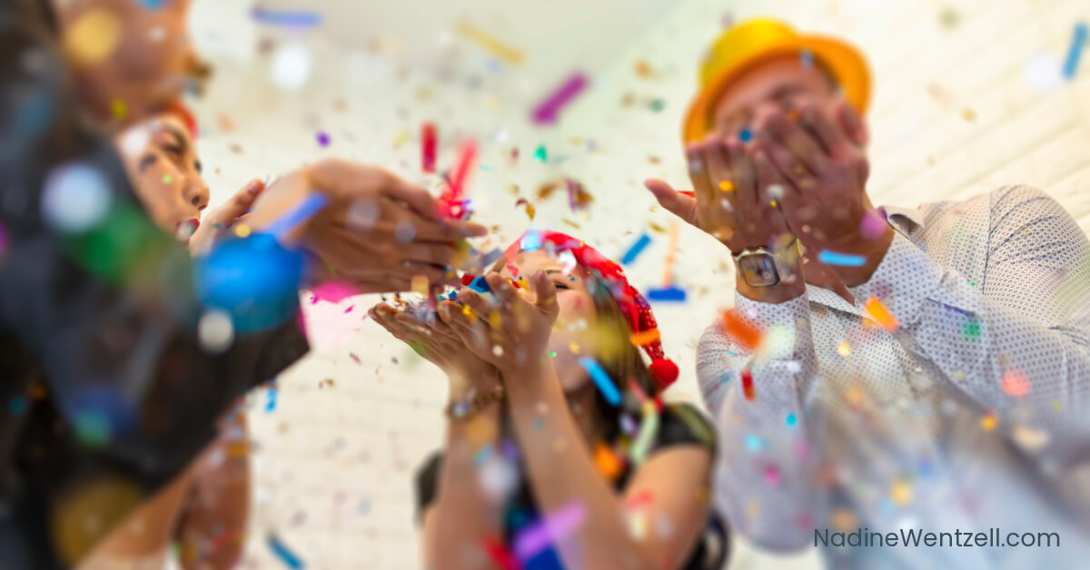 People celebrating at a festive event, joyfully blowing colorful confetti into the air. The vibrant scene captures a sense of fun and camaraderie, with bright decorations and cheerful energy.